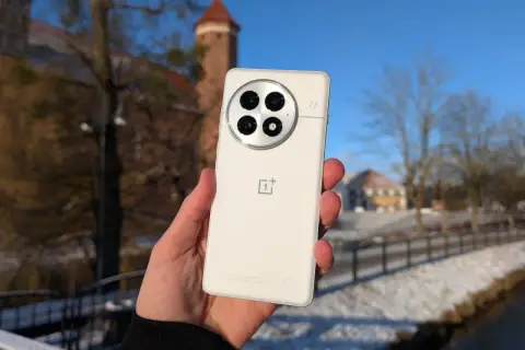 Biały smartfon z charakterystycznym modułem aparatów, trzymany na tle zimowego krajobrazu z zamkiem. System Oxygen OS działa płynnie.